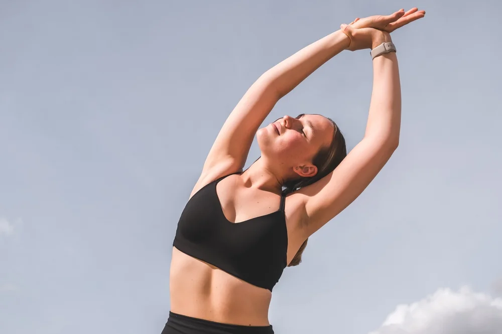 A woman stretches her arms overhead while exercising outdoors - Chiropractor Flower Mound TX